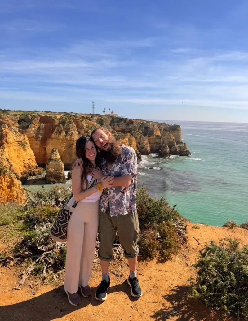 Benjy and Sofia laughing together on a clifftop above the Atlantic