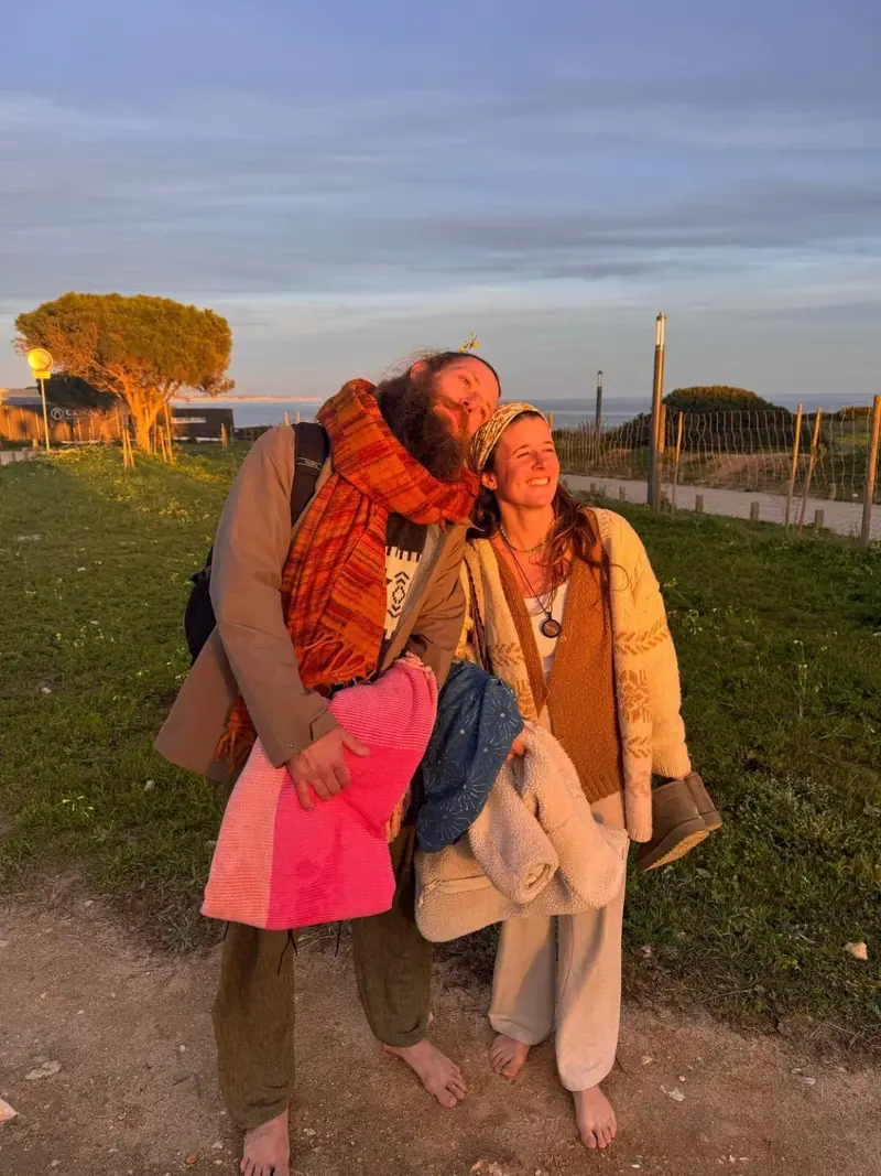 Benjy and Sofia standing barefoot on grass in low evening light near the coast