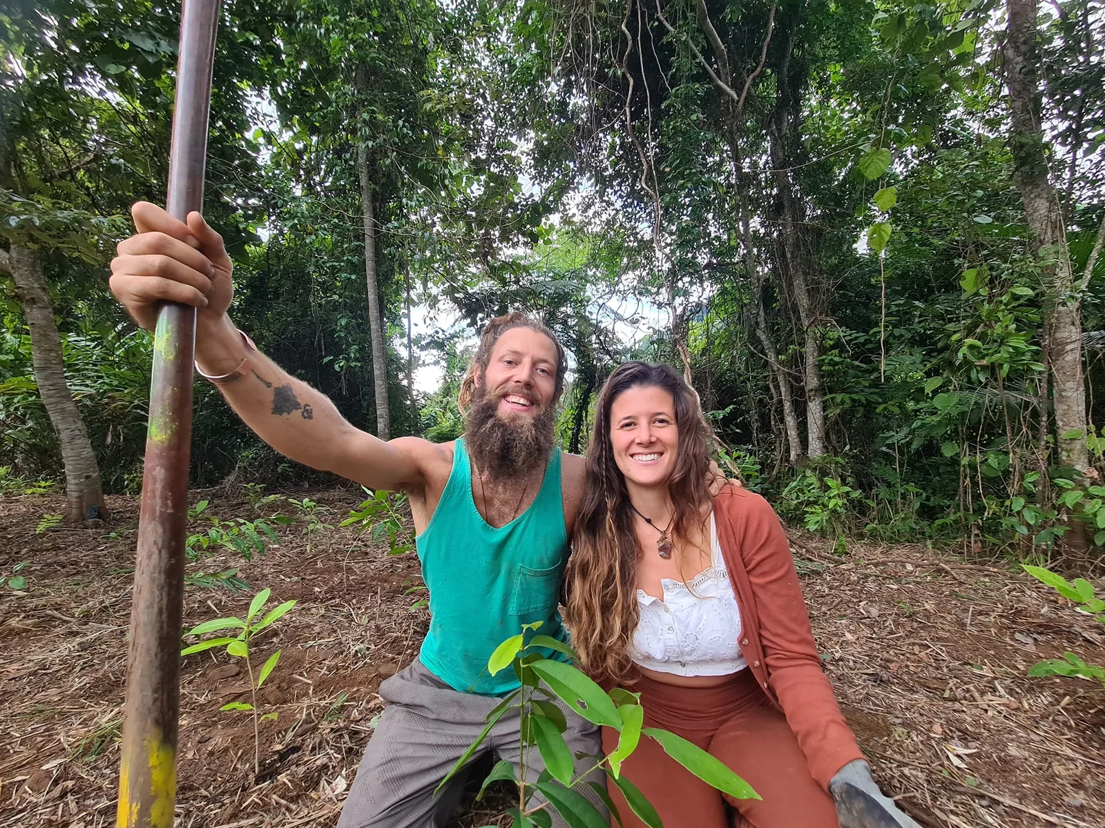 Benjy and Sofia smiling beside a young tree in a food forest